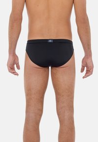 Černé plavky z hladké tkaniny. Mají klasický střih, který se přizpůsobuje postavě, a decentní značkovou etiketu na zadní části pasu.