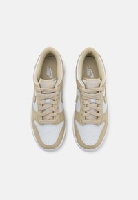 Baskets Nike marron clair et blanches avec une tige en cuir, un bout perforé et des lacets texturés, arborant le logo Nike sur la languette.