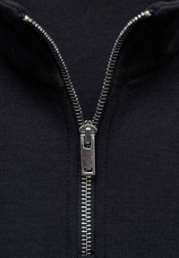 Zwart kledingstuk met ritssluiting, gekenmerkt door een metalen rits met een zilveren trekker, dat een gladde textuur en een nauwsluitend ontwerp laat zien.