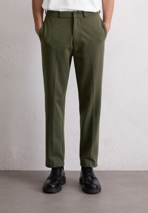 Olijfgroene op maat gemaakte broek met een gladde textuur, een platte voorkant en zijzakken, gecombineerd met zwarte veterlaarsjes.