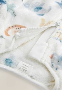 Kocyk niemowlęcy z mikrofibry w białej podstawie z kolorowymi wzorami zwierząt, z zamkiem błyskawicznym z boku oraz etykietą z napisem "NEXT Baby."
