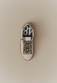 Baskets blanches avec lacets et talon à rayures tigre, semelle marron clair et semelle intérieure noire affichant le numéro 48 en blanc.
