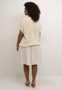 Beige short-sleeve top made of lightweight fabric, paired with a light cream, knee-length skirt. Model wearing soft gold slide sandals.