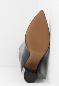 Grå højhælet sko med øvre del i tekstureret læder, spids tå og brun flad sål. Mærke og størrelse trykt på sålen.