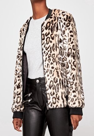 Veste en fausse fourrure imprimé léopard avec poignets côtelés noirs portée sur un haut gris clair et un pantalon en cuir noir avec des détails zippés.