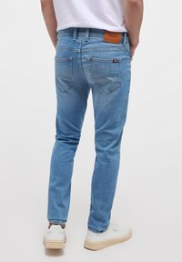 Heledad sinine teksaseelik, slim fit lõikega, viie tasku disainiga ning pruuni nahast lapiga vööl. Omab kaarekujulisi tagataskuid.