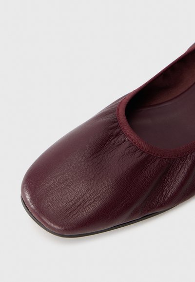 Ballerine en cuir bordeaux avec un bout rond et un bord élastiqué. Texture lisse et design minimaliste, avec un profil bas.