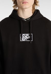 Felpa nera con cappuccio e logo "VANS" ricamato bianco, dotata di cordoncino e un tessuto morbido e texturizzato.