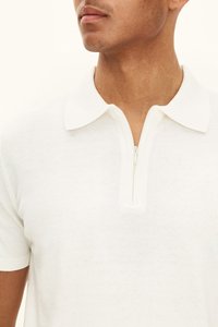 Valkoinen vetoketjullinen poolopaita, jossa on pehmeä pinta, lyhyet hihat ja klassinen kaulus. Edessä vetoketju sulkemista varten ja saumaton muotoilu.