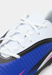 Κοντινή λήψη ενός λευκού αθλητικού παπουτσιού με μαύρες και μπλε λεπτομέρειες και λευκές κορδόνες δεμένες σε απλό φόντο.