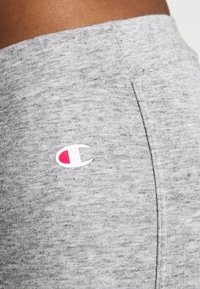 Leggings grigi in tessuto morbido e testurizzato. Presentano un piccolo logo bianco con accenti rosa sul lato. Dettagli delle cuciture visibili.