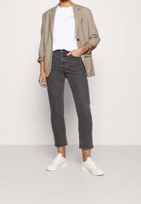 Beige blazer over en hvid t-shirt, kombineret med sort højtsiddende jeans og hvide sneakers. Indeholder skræddersyet snit og op-rullede ærmer.