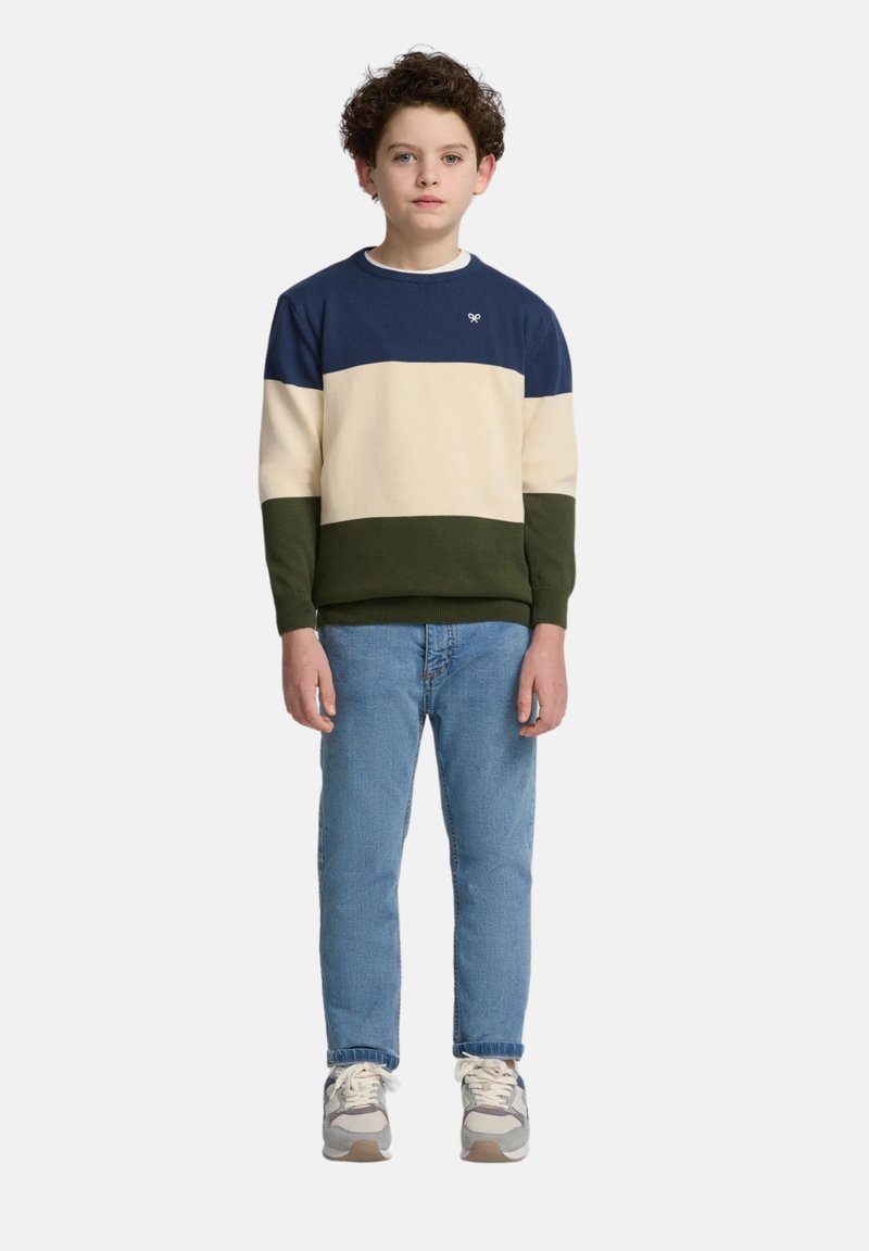 Suéter con bloques de color en azul marino, crema y verde. Material de punto, cuello redondo, con puños acanalados. Combinado con jeans azul claro y zapatillas.