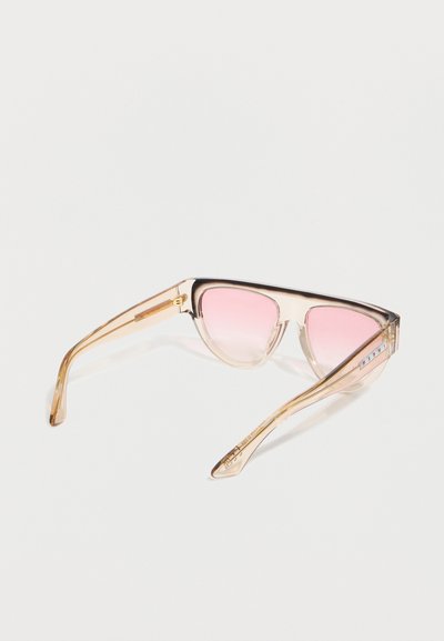 Διαφανή γυαλιά ηλίου σε σχήμα γάτας σε μπεζ χρώμα με ροζ φακούς με διαβάθμιση και λεπτές χρυσές μεταλλικές λεπτομέρειες στα πλαϊνά.