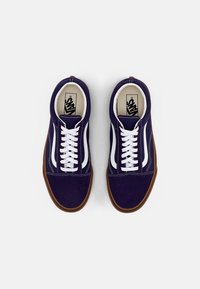 Pár námořnických modrých tenisek Vans s bílým bočním pruhem, bílými tkaničkami a gumovými podrážkami, z pohledu shora na bílém pozadí.