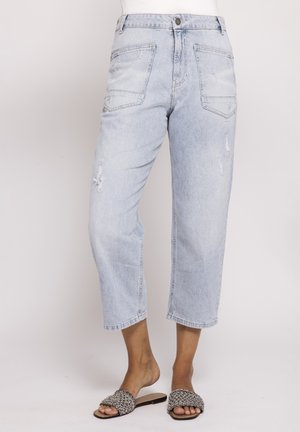 Light wash cropped jeans with front patch pockets and distressed details, worn with black and white woven slide sandals.