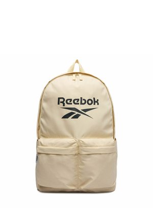 Béžový batoh Reebok s černým logem, dvěma předními kapsami na zip a horním uchycením na bílém pozadí.