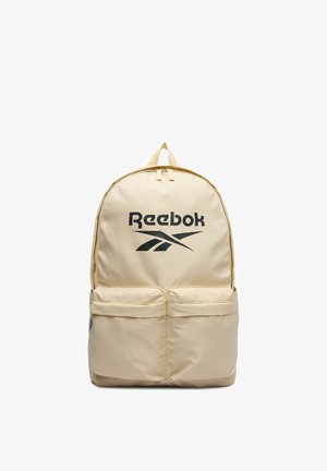 Beżowy plecak Reebok z czarnym logo, dwiema przednimi kieszeniami na zamek i górnym uchwytem na białym tle.