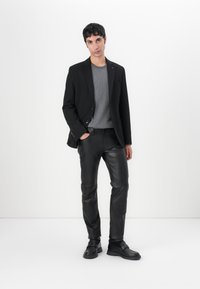 Šedý sveter pod čiernym blazerom, doplnený čiernymi koženými nohavicami a čiernymi topánkami. Outfit sa vyznačuje čistými líniami a prispôsobeným strihom.