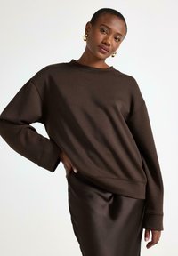Brun oversized sweatshirt med drop shoulders, rund hals och strukturerad tyg, kombinerad med en elegant brun satin kjol.