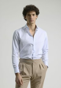 Camisa de dress de rayas azul claro y blanca, hecha de algodón, con cuello extendido y mangas largas, combinada con pantalones beige con pliegues.