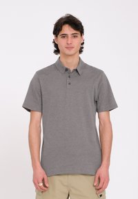 Polo shirt gris à manches courtes avec col, trois boutons et un petit logo. Texture lisse, coupe décontractée et design épuré.