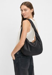 Borsa hobo in pelle nera con una forma morbida e arcuata e una singola tracolla. Presenta un logo del marchio discreto sulla parte anteriore.