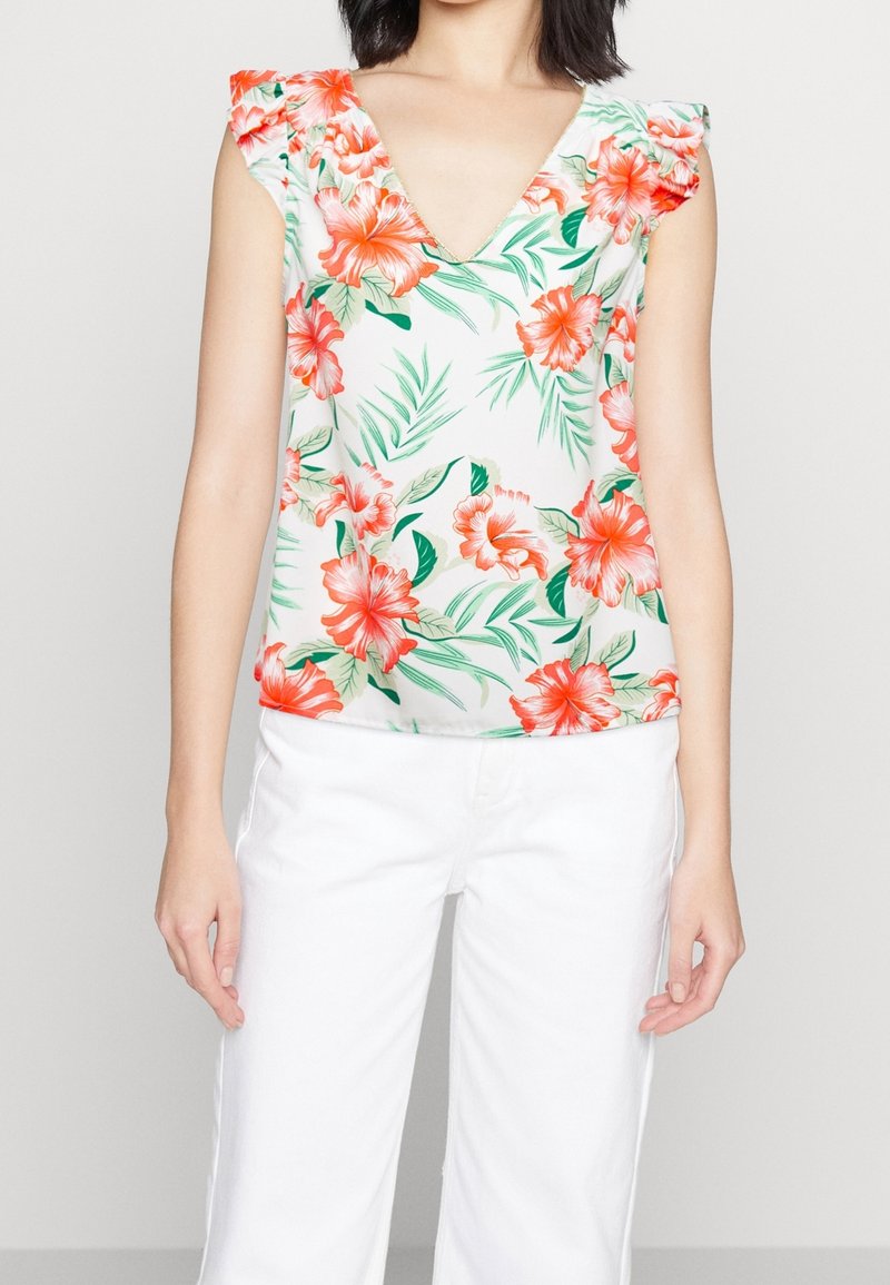 Débardeur floral avec un décolleté en V, présentant des fleurs d'hibiscus orange et rose sur fond blanc, associé à un pantalon blanc.