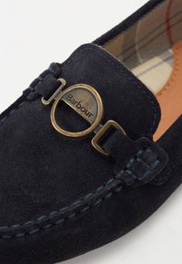 Tumesinine suede slip-on kingad, millel on ümberringi messingist aksent, millel on graveeritud "Barbour", kontrastne sinine niit ja siseplaid vooder.