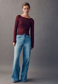 Bordo dugih rukava s teksturiranim uzorkom uparen s svijetloplavim trapericama širokih nogavica. Jednostavan dizajn s pripijenim krojem i suptilnim sjajem.