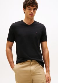 Svart kortärmad t-shirt med v-ringning i bomull, med en liten logga på bröstet, kombinerad med beige byxor.