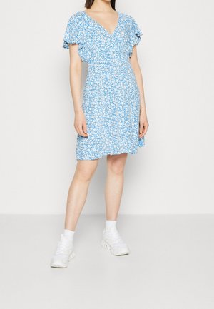 Robe courte bleue avec motif floral, encolure en V, manches courtes volantées, taille froncée, longueur au-dessus du genou, associée à des baskets blanches.