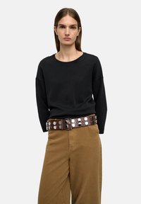 Czarna bluzka z długim rękawem i okrągłym dekoltem, połączona z brązowymi spodniami oraz szerokim brązowym paskiem z srebrnymi okrągłymi ćwiekami.