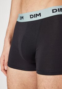 Sorte bomullsboxershorts med en lys blå elastisk linning som har merkevarenavnet "DIM" i svart skrift. Strukturert stoff, tettsittende design.