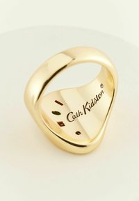 Zelta toni gredzens ar gludu, viļņotu formu; iekļauts embosēts "Cath Kidston" logos un mazi krāsaini akcenti iekšpusē.