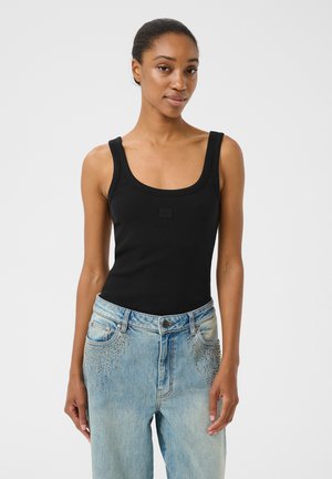 Canotta nera a coste con spalline larghe e scollatura a girocollo, abbinata a jeans blu sbiaditi con dettagli borchiati sulle tasche.
