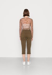 Blusa transparente de mangas longas com padrão de leopardo castanho, combinada com calças capri em verde-oliva e ténis brancos. Design simples e ajustado.