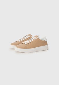Baskets en cuir tan avec des lacets et des semelles blanches. Design minimaliste avec une texture lisse et un logo subtil sur le côté.