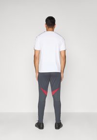 Hvid træningsskjorte og grå leggings med røde accenter. Leggings har en tætsiddende pasform og sidelængder; skjorten har korte ærmer og en rund hals.