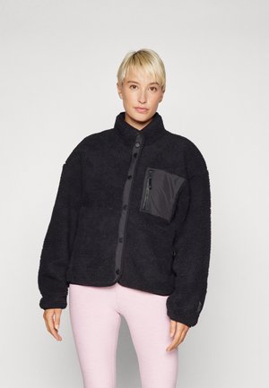 Veste en polaire texturée noire avec un col montant, fermeture à boutons sur le devant et une poche poitrine zippée en tissu lisse.