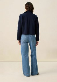 Marineblauw cropped jasje met een grote kraag, gecombineerd met hooggesneden lichtblauwe wijde spijkerbroek met achterzakken en rafelige zomen.