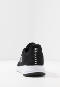 Zwarte sport schoen met een bovenwerk van mesh, witte zool en een getextureerde hiel met herhaalde logo. Achteraanzicht toont een gewatteerde kraag.