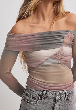 Kobieta ubrana w pastelowy ombre top z marszczeniami, odkrywający ramiona, z długimi przezroczystymi rękawami i jasnoszare, wysokowpasowane dżinsy.