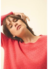 Helles pinkes Strickpullover mit lockerer Passform und geripptem Ausschnitt, mit weicher Textur und losen Ärmeln, getragen von einem Model.