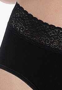 Schwarze Unterwäsche mit einem Spitzenrand an der Taille, mit einer glatten Textur und einer klassischen Slip-Form. Die Spitzenakzente verleihen dekorative Details.