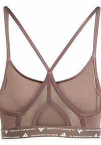 Športová podprsenka v mauve farbe s priesvitným zadným dielom a krížovými ramienkami. Obsahuje elastický pás so značkou a opakujúcim sa textom. Mäkka, hladká textúra.