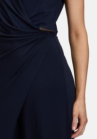 Robe bleu marine au design drapé, avec un détail torsadé à la taille et un accent métallique pour ajouter de la texture.