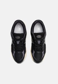 Chaussures de course noires avec tige en mesh et daim, présentant un design texturé et des accents gris, lacets ronds, et une semelle extérieure en caoutchouc.