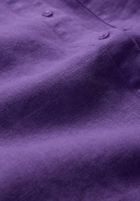 Violet linas audinys su matomomis tekstūromis ir subtiliu blizgesiu, apipavidalintas mažomis atitinkamomis sagomis uždarymui. Minkštas ir lygus paviršius.