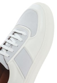 Baskets blanches avec des accents gris clair, en cuir lisse, à bout rond, avec des lacets blancs plats, des coutures contrastantes et un collier rembourré.